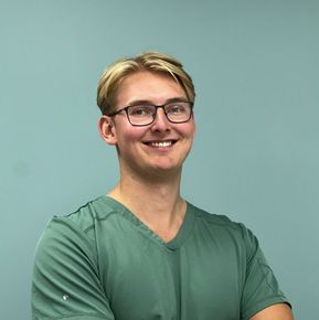 Tannlege Christian med briller og skjegg, iført blå skjorte og medisinsk maske, smiler til kameraet.