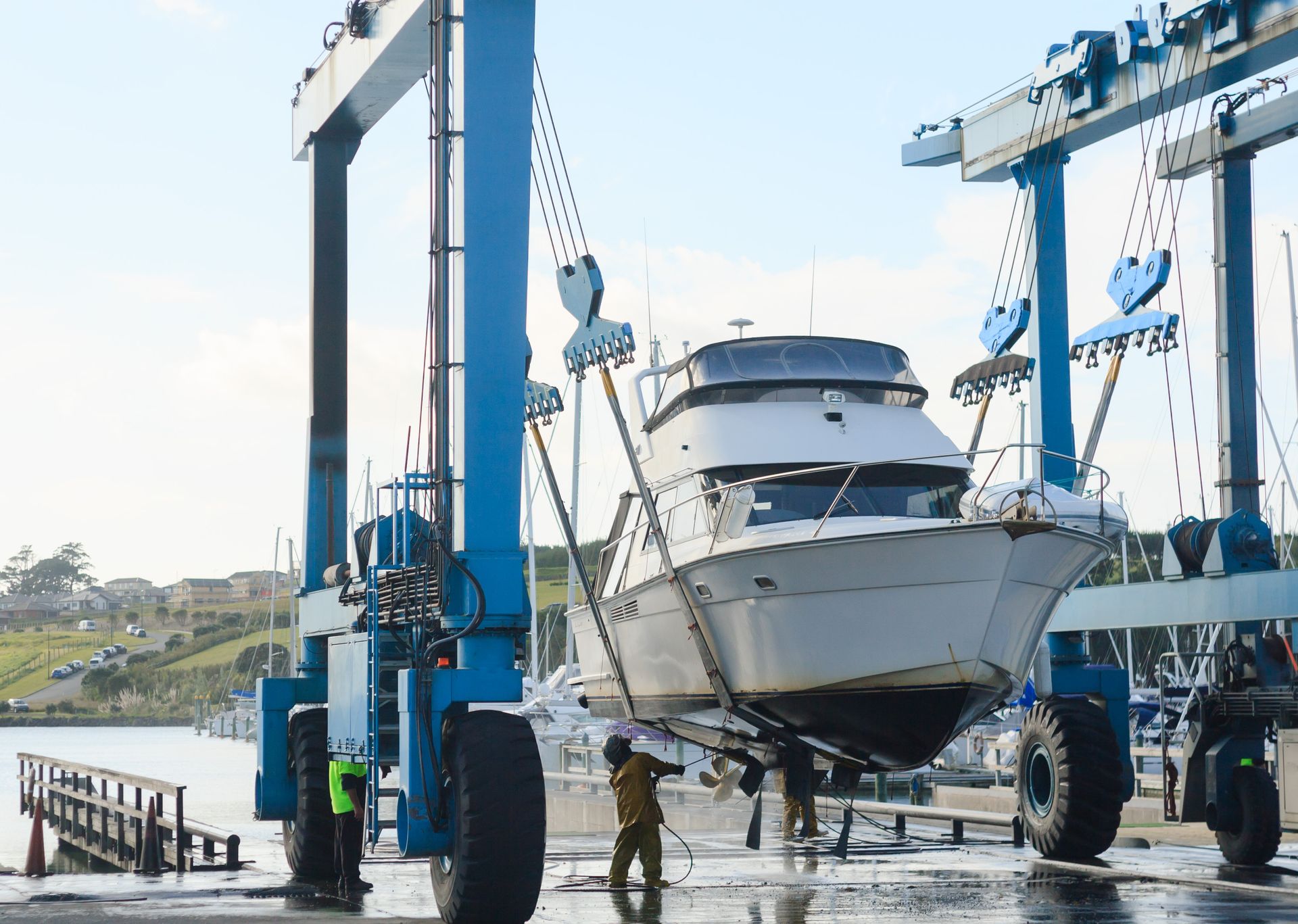 A white yacht being lifted by a blue boat hoist at a harbor.