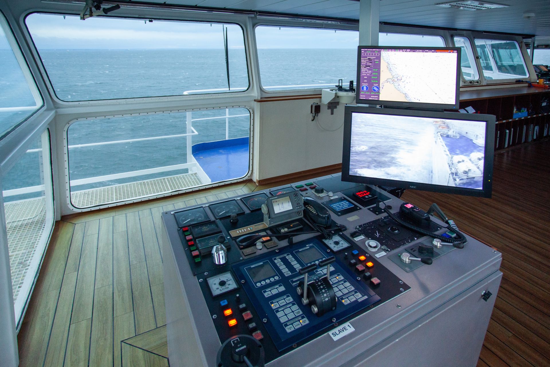 Bridge of a ship with navigation displays and control panel, overlooking the ocean.