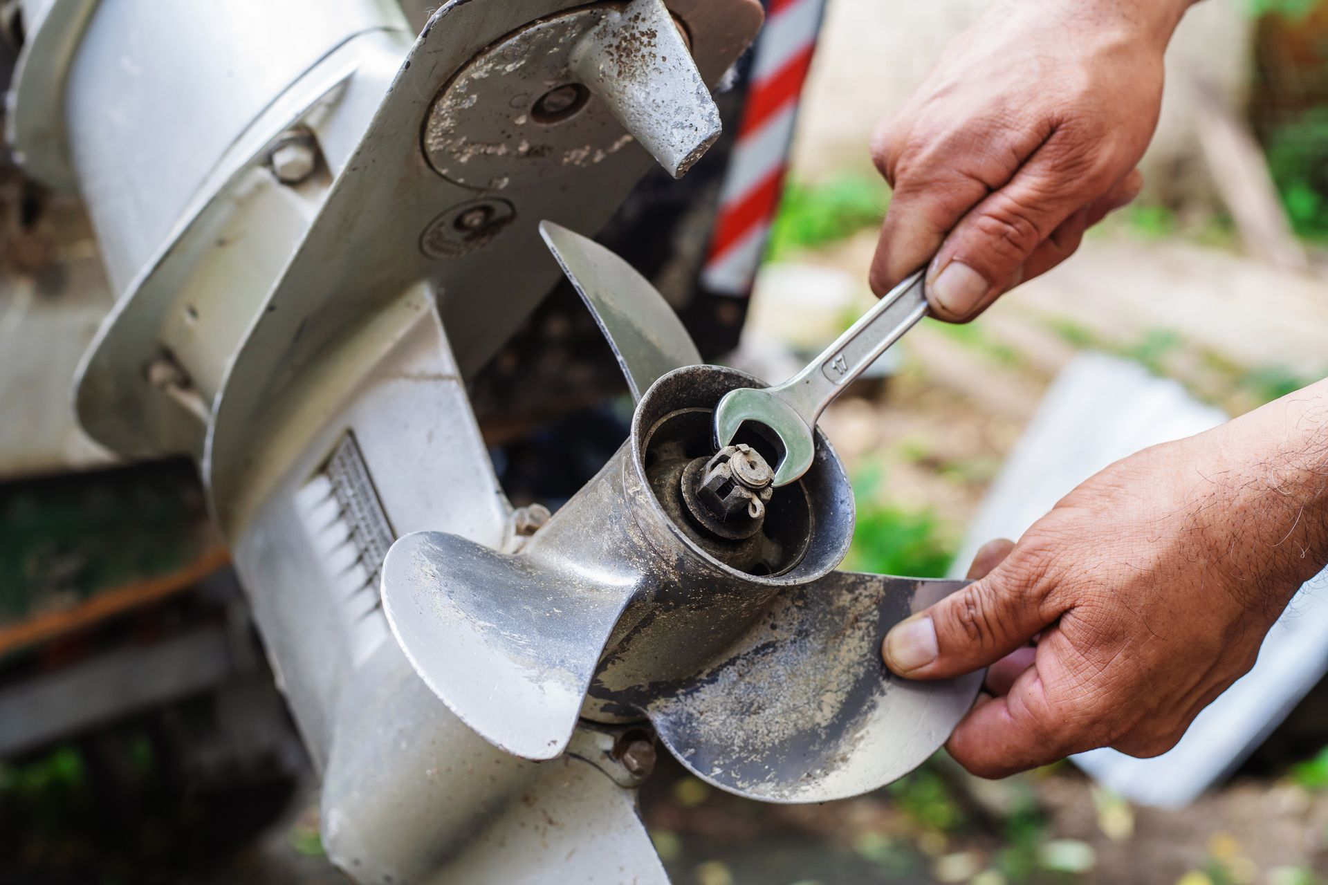 Hands using a wrench to remove the propeller from an outboard motor.