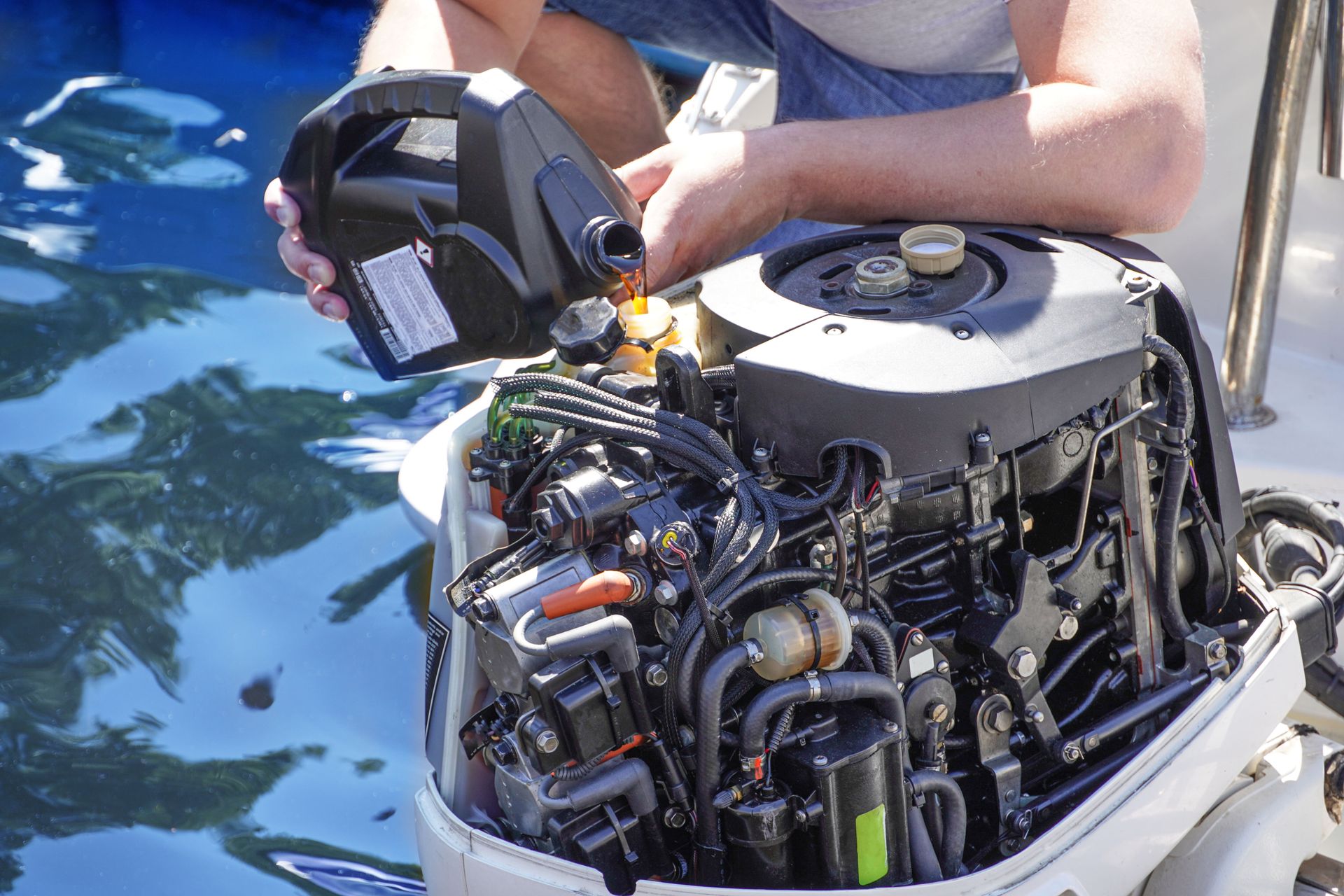 Person pouring oil into a boat engine. Water surrounds the boat.