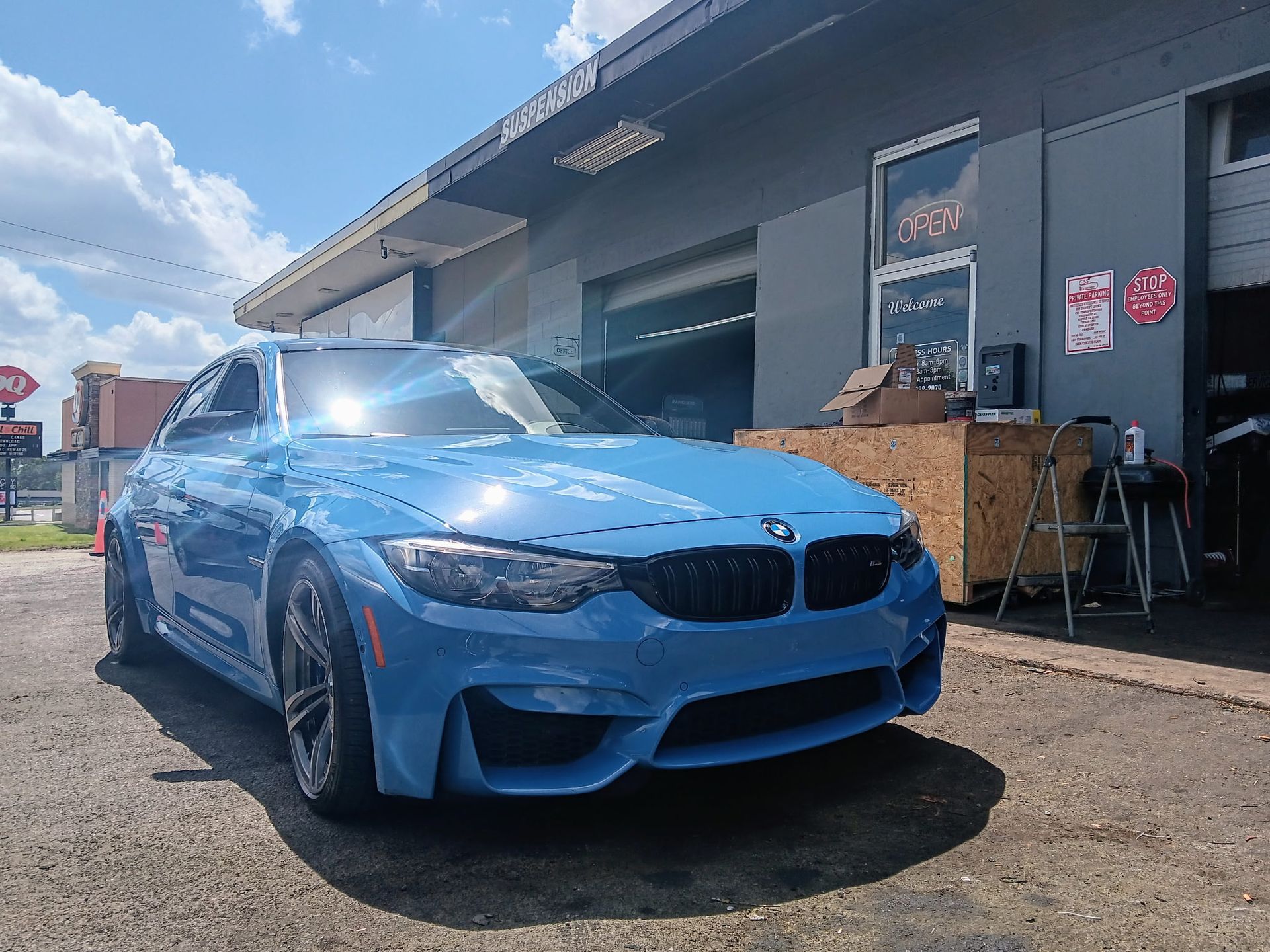 Blue BMW sports car parked in front of a repair shop on a sunny day.