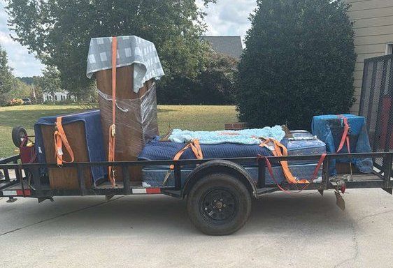 Trailer loaded with covered furniture and boxes parked on a driveway