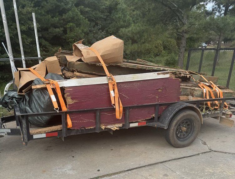 Loaded utility trailer with wooden furniture and debris strapped down on a roadside.