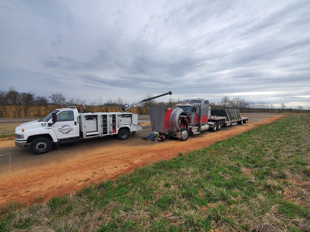 A tow truck is parked on the side of a dirt road next to a field.