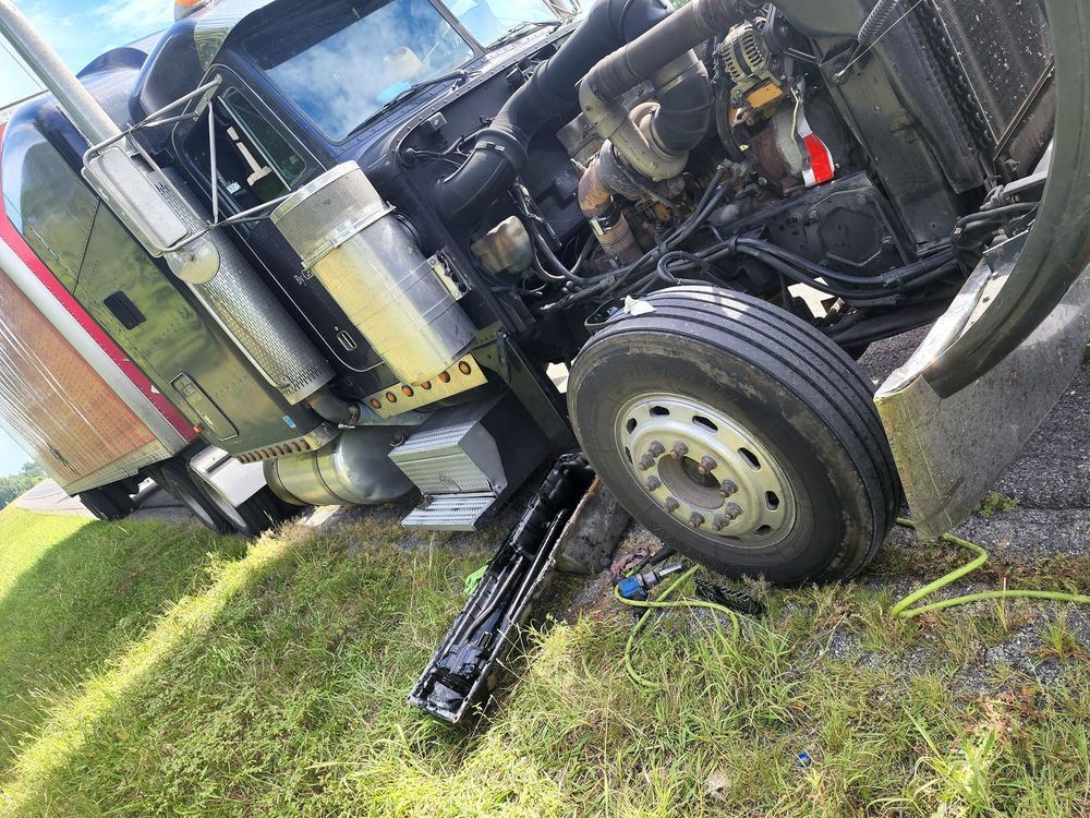 A semi truck is laying on its side on the side of the road.