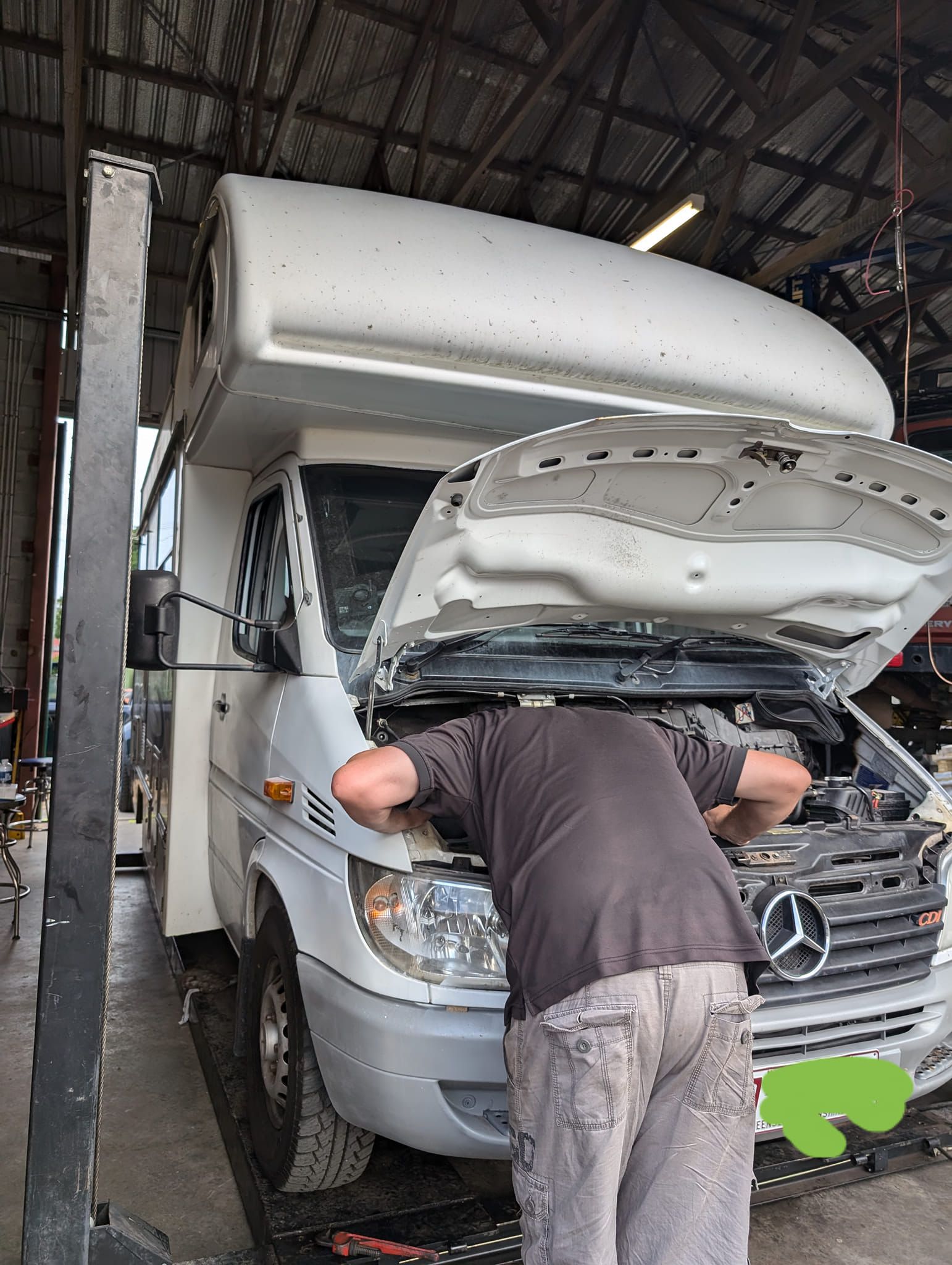Three people working on a black van with the hood up outdoors; one person under the van.