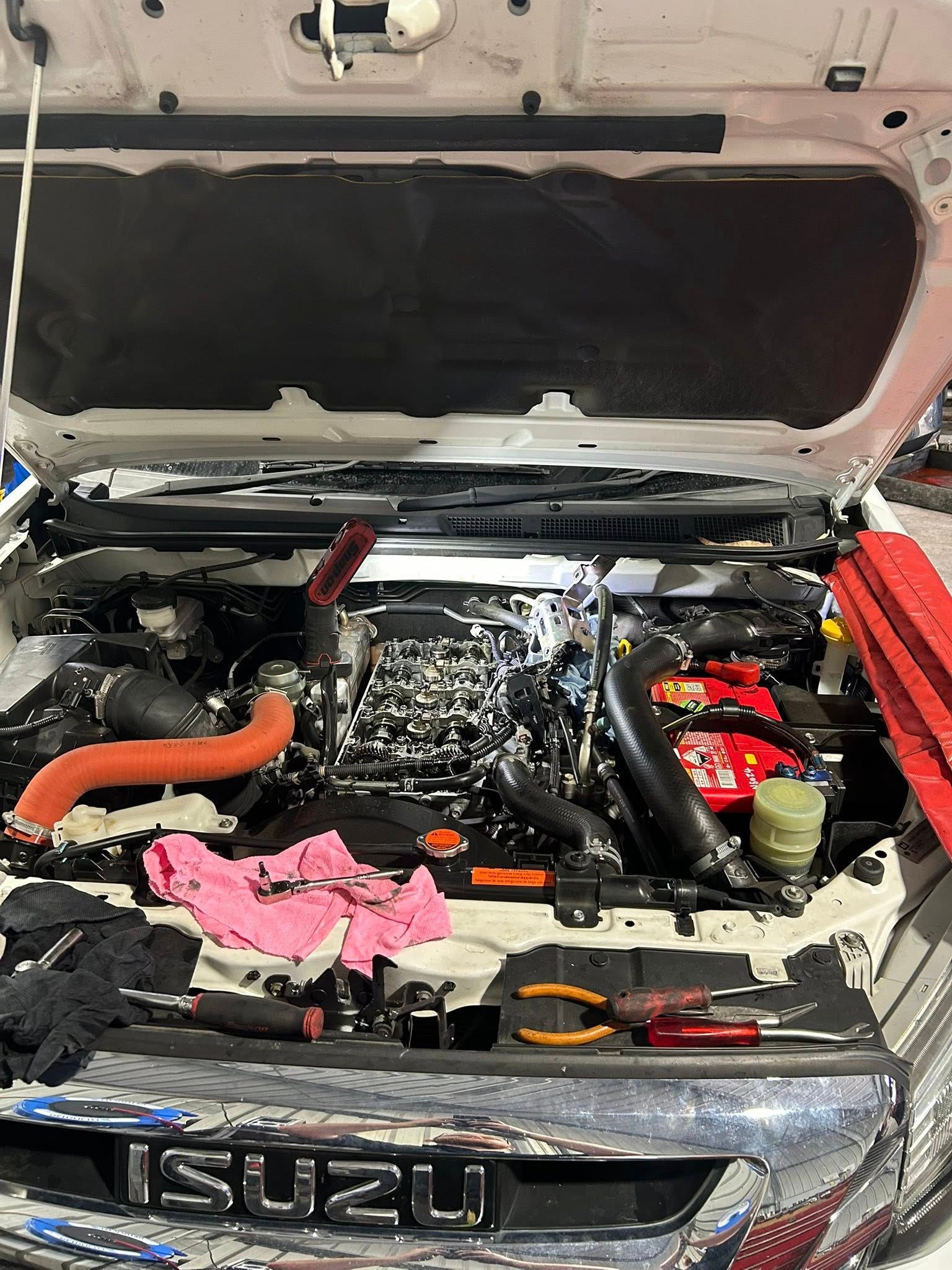 An Isuzu truck engine bay is open, with tools and components scattered around.