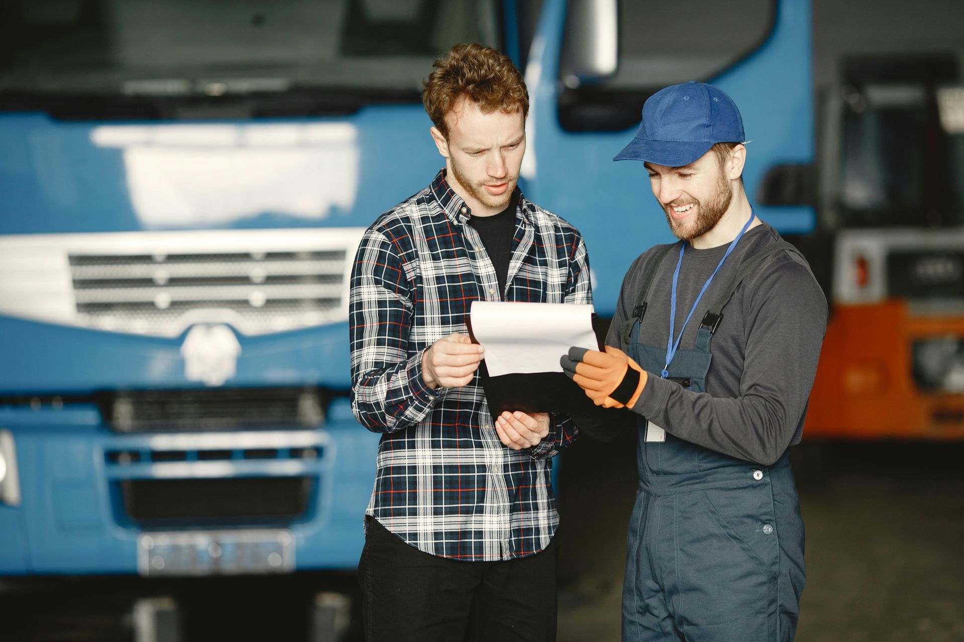 Mechanic in blue jumpsuit, wearing gloves, working on a car's exposed gears in a garage.