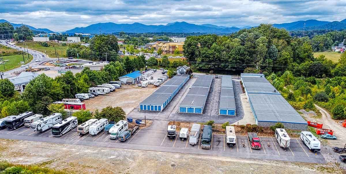 Aerial view of a self-storage facility with RV and vehicle parking against a backdrop of trees and distant mountains.