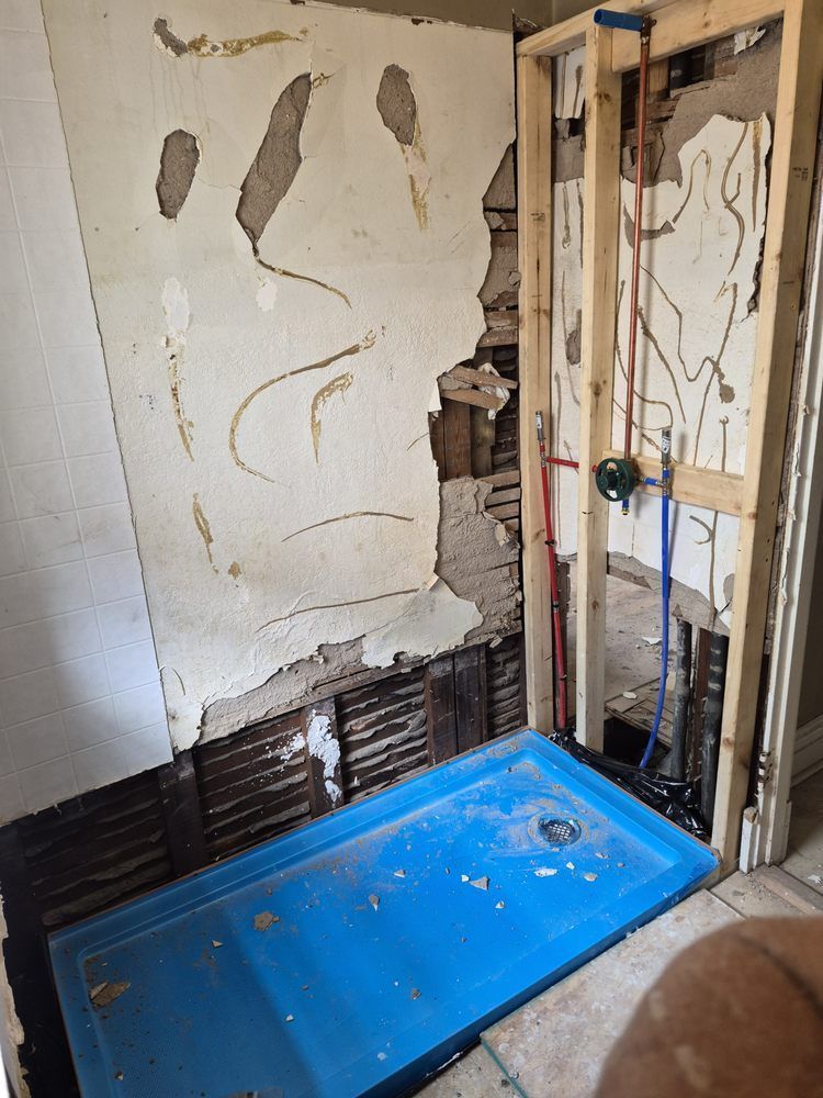 Damaged bathroom wall with exposed studs and a blue shower base during renovation
