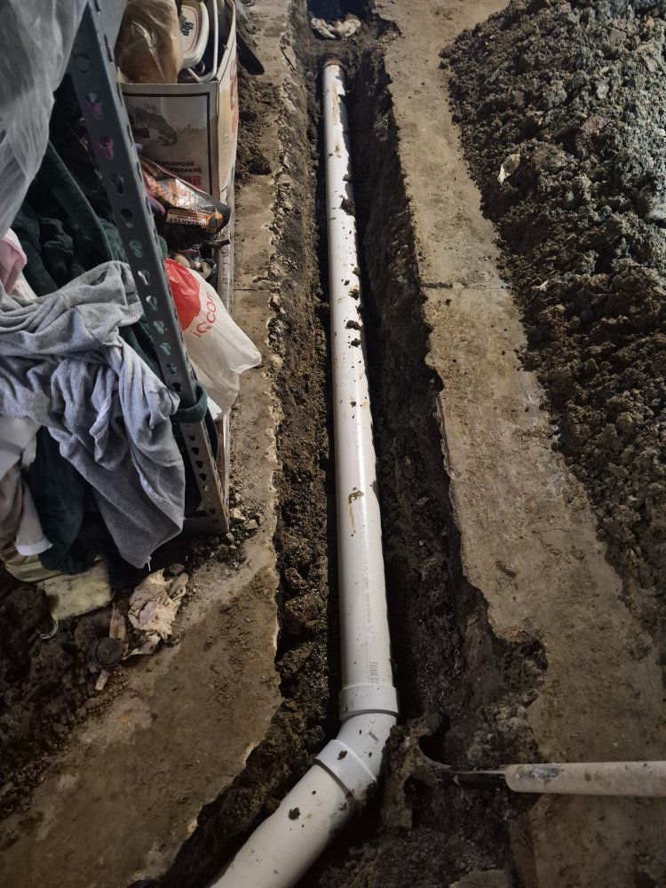 Trench with a white PVC pipe installed in dirt beside a wall and construction debris