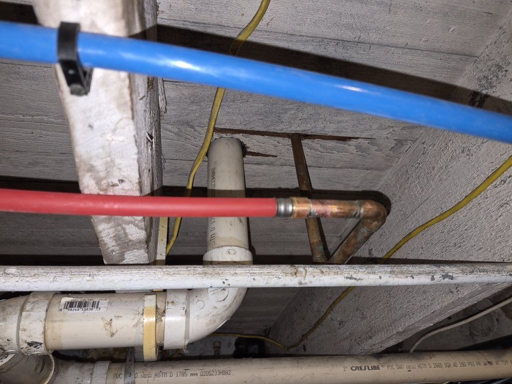 Exposed red, blue, and white pipes and conduit running along a concrete ceiling.