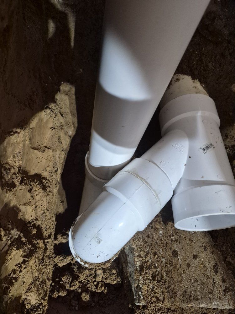 White PVC drain pipes joined in a trench beside dirt and concrete.