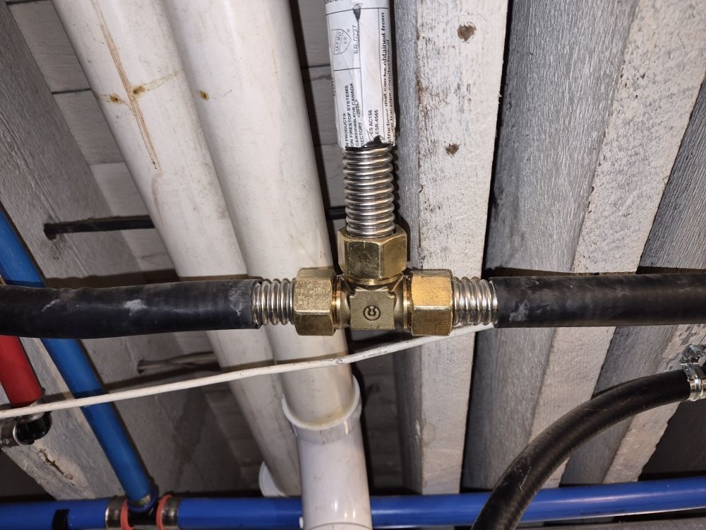 Brass pipe valve with black and white pipes against a corrugated metal ceiling