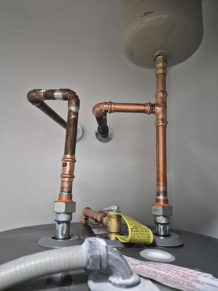 Copper sink pipes and fittings beneath a bathroom sink, with a gray drain hose and shutoff valve.