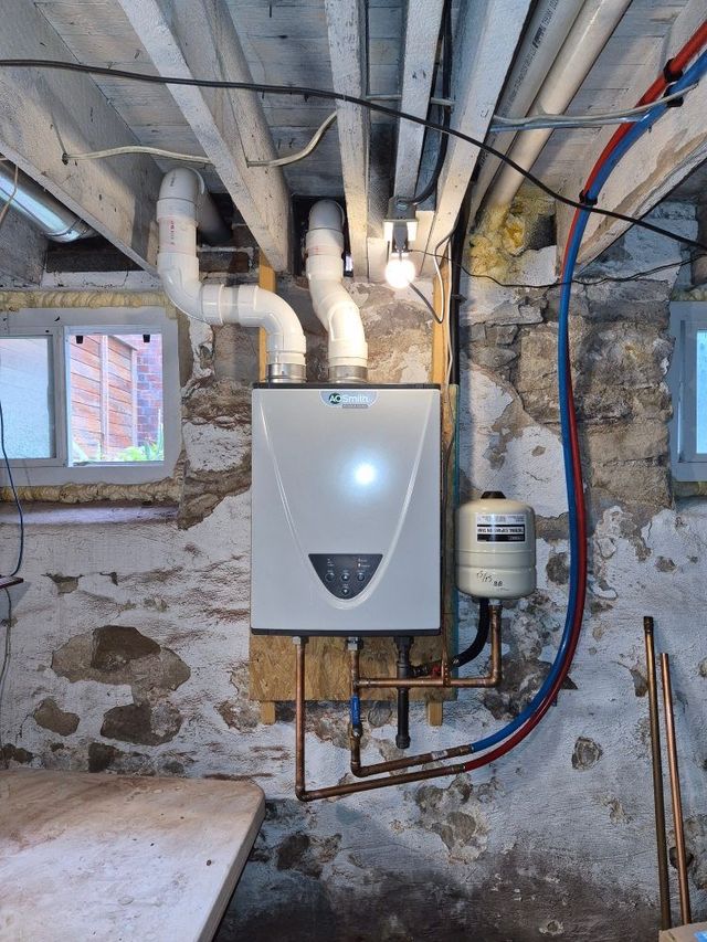 Basement utility room with a wall-mounted boiler, exposed pipes, and stone foundation walls