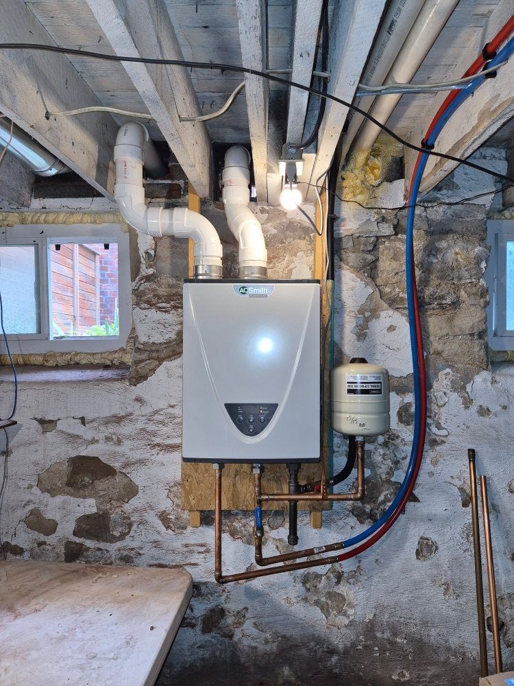 Basement utility room with a wall-mounted boiler, exposed pipes, and unfinished stone walls.