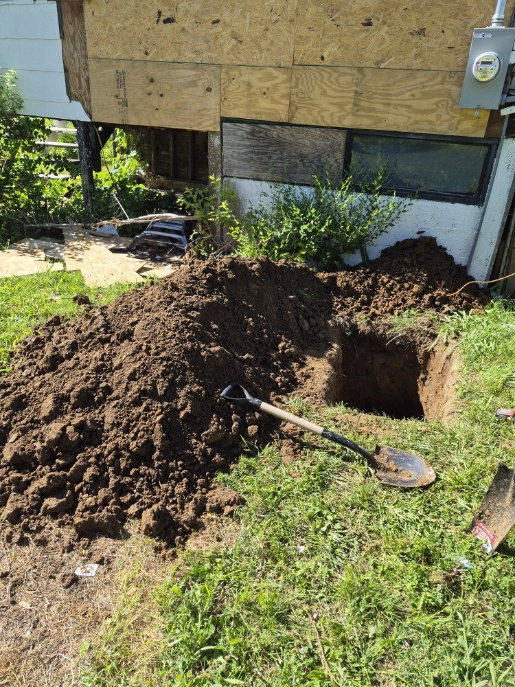 Large dirt pile beside a house with a shovel and a freshly dug hole in the yard