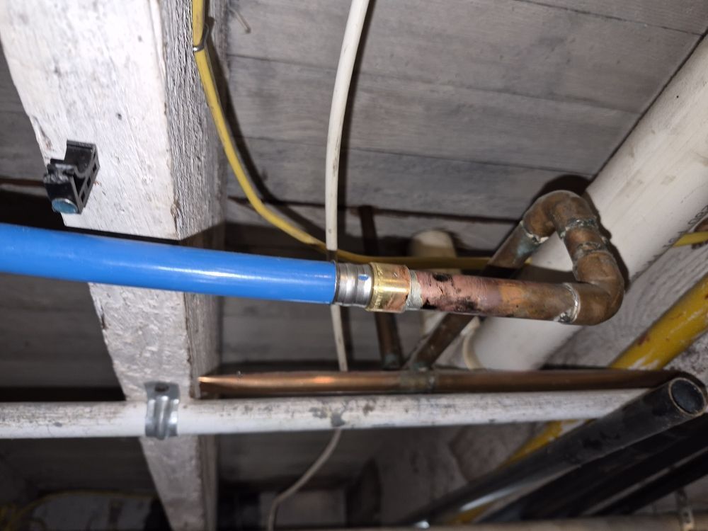 Blue and copper pipes connected under a wooden floor