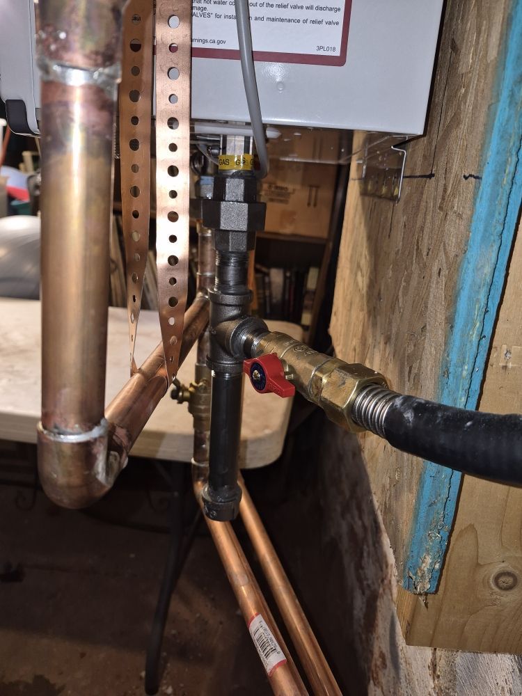 Copper pipes and a red-handled valve in a cramped utility space beside a water heater.
