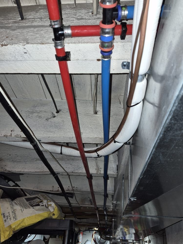Red and blue utility pipes run along a low basement ceiling with exposed concrete and wiring.