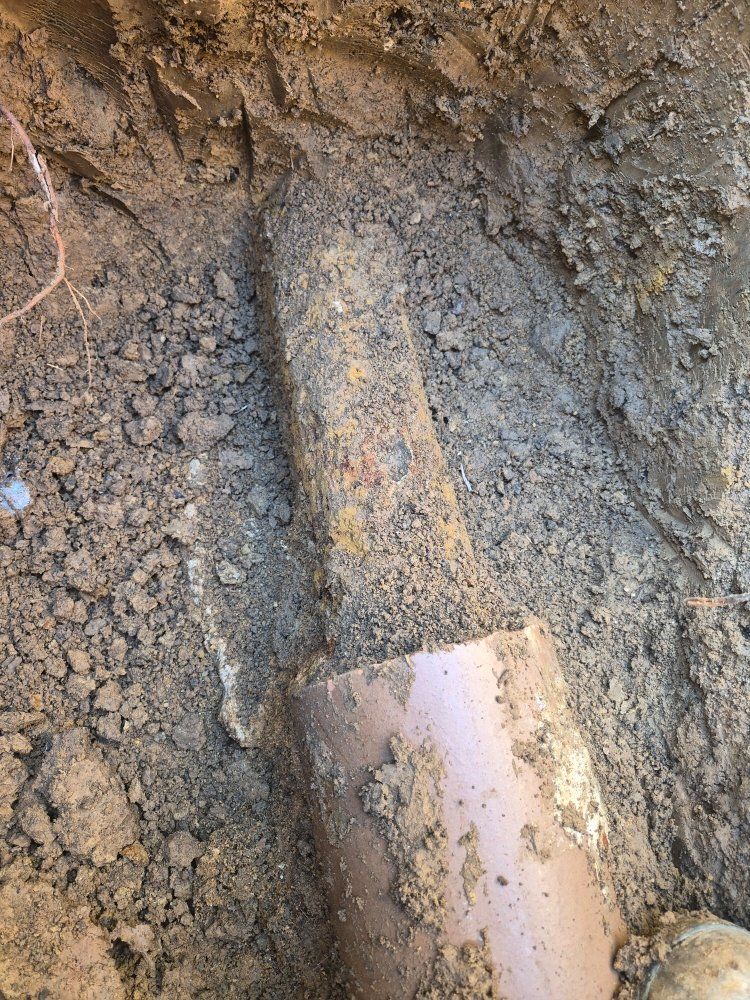 A muddy metal pipe partially buried in soil, with a cut end exposed near the bottom.