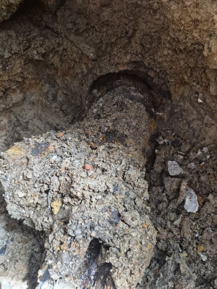 Dirt-packed excavation hole with a buried pipe end and debris inside
