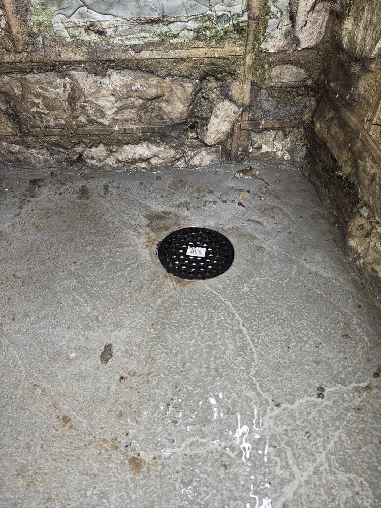Stone floor corner with a black drain cover against rough stone walls.