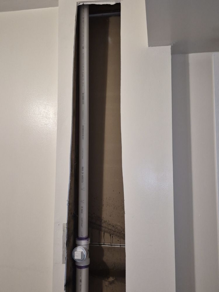 Open wall niche with exposed vertical pipe and conduit in a white interior wall.