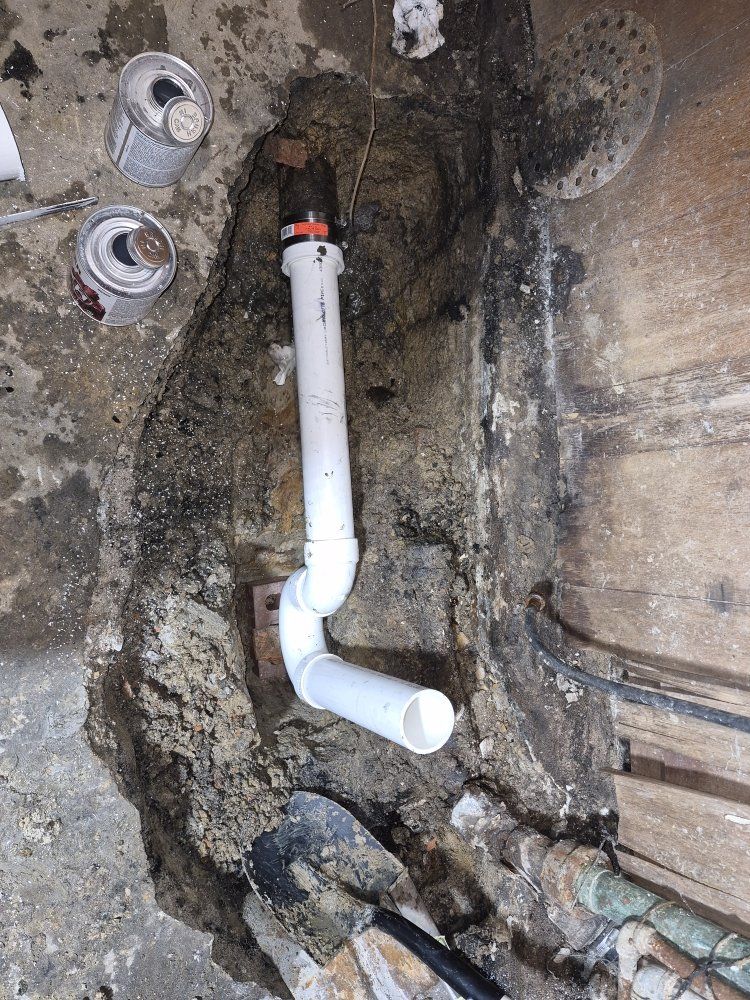 White PVC drain pipe with elbow joints mounted in a rough concrete wall cavity near exposed plumbing connections