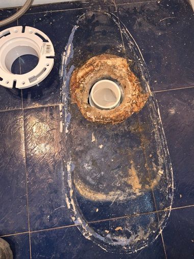 Rust-stained toilet base on a dark blue floor, with a circular pipe opening nearby.