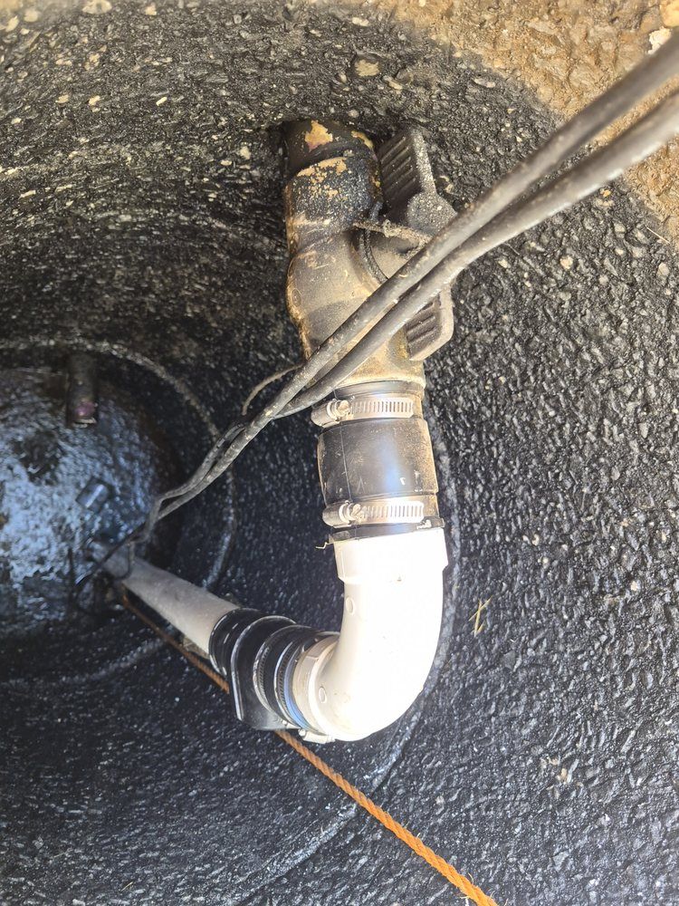 Close-up of a black pipe and white elbow fitting on a rough concrete surface, with cables running across it.