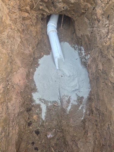 PVC pipe pouring gray cement into a dirt trench