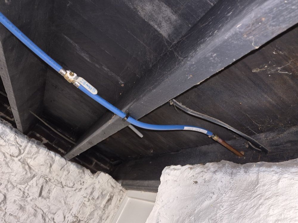 Blue cable running across a dark ceiling above rough white brick walls