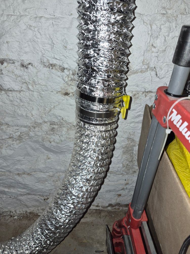Flexible silver duct hose beside a red Milwaukee tool on a rough wall surface