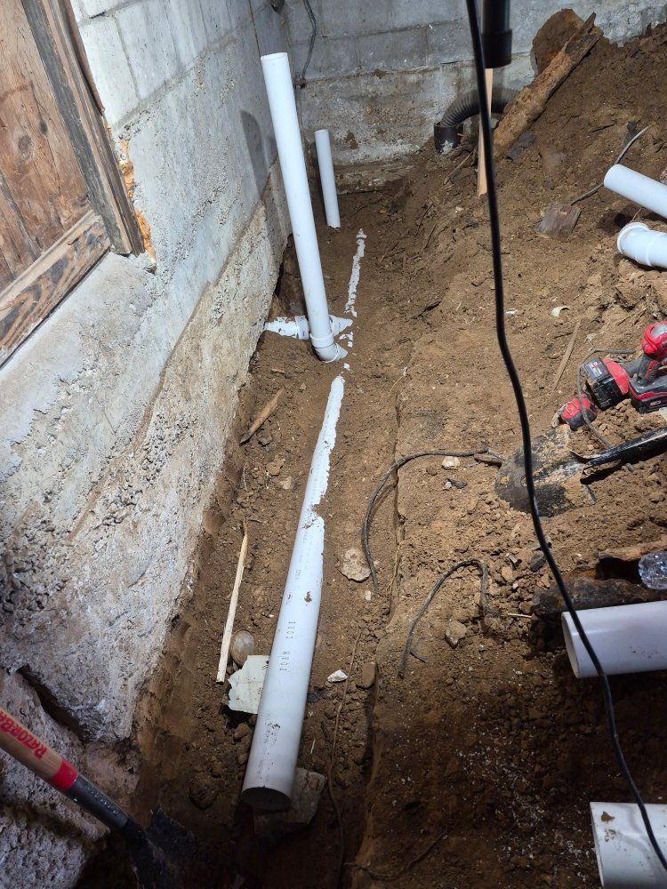 Basement construction area with white PVC pipes, dirt floor, and tools near a cinderblock wall