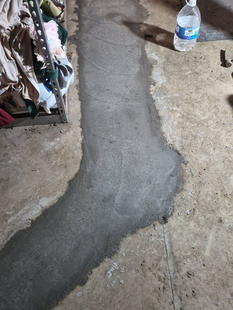 Fresh gray concrete patch running through a rough floor beside a water bottle and cluttered items