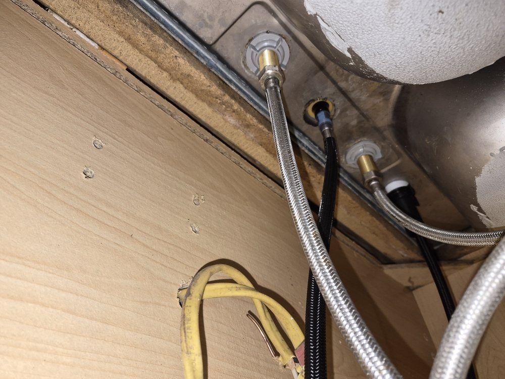 Braided hoses and wires beneath a sink or appliance against a wood panel background