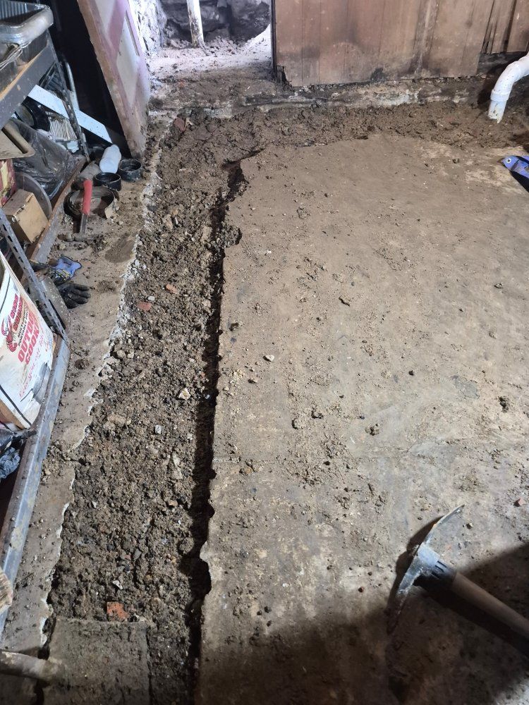 Freshly dug trench beside a concrete slab in a construction area, with tools and debris nearby