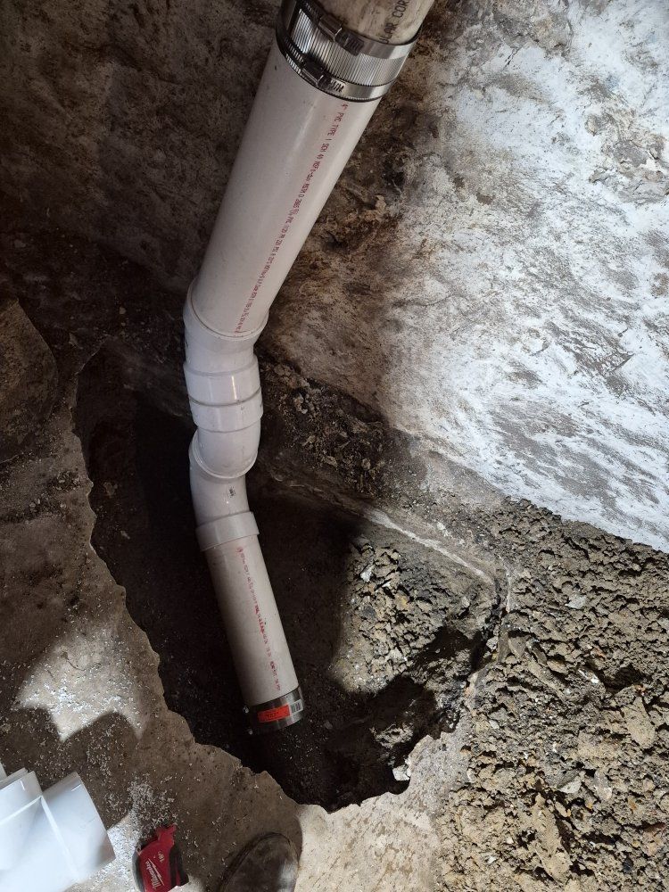White PVC pipe in a dirt hole near a rough wall during plumbing work