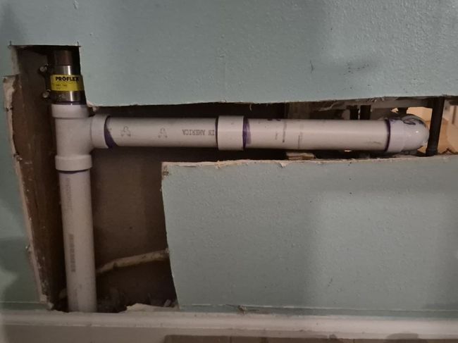 Exposed white PVC plumbing pipes running through a wall opening during repair