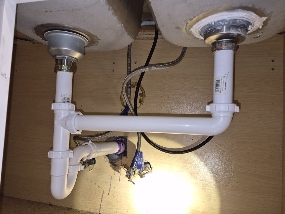 Under-sink plumbing with two white drain pipes and a loose black wire in a cabinet opening