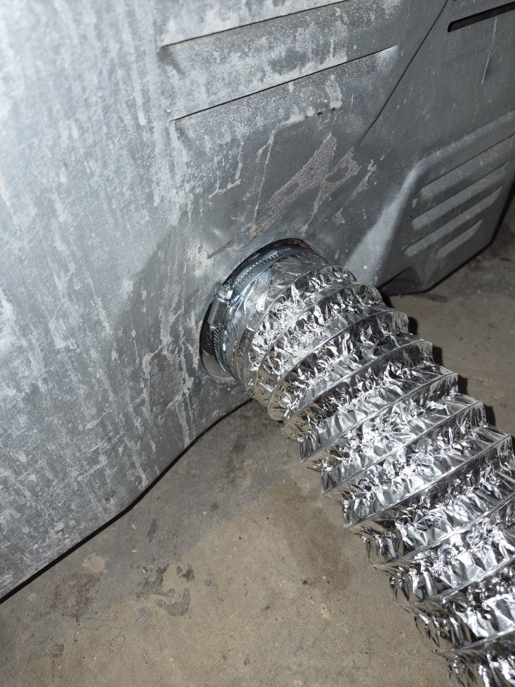 Silver flexible duct connected to a metal vent opening on a gray appliance.