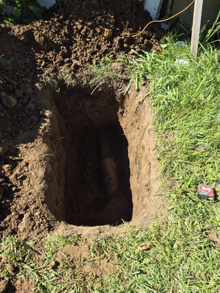 Freshly dug rectangular hole in a grassy yard with soil piled around it