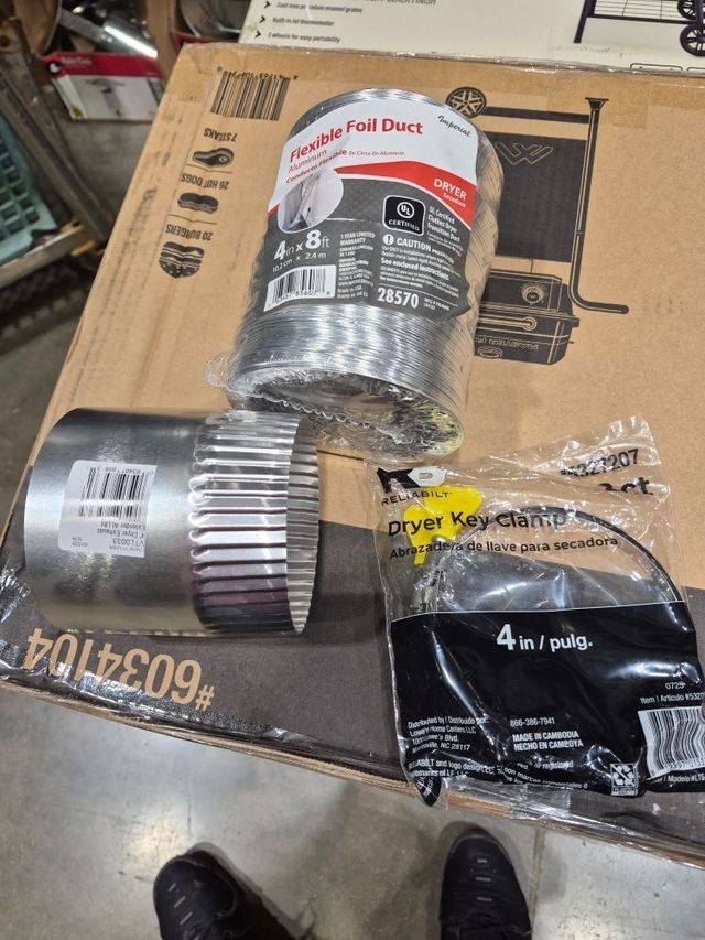 Box of HVAC duct parts and a black 4-in. poly bag on a cardboard box in a workshop.