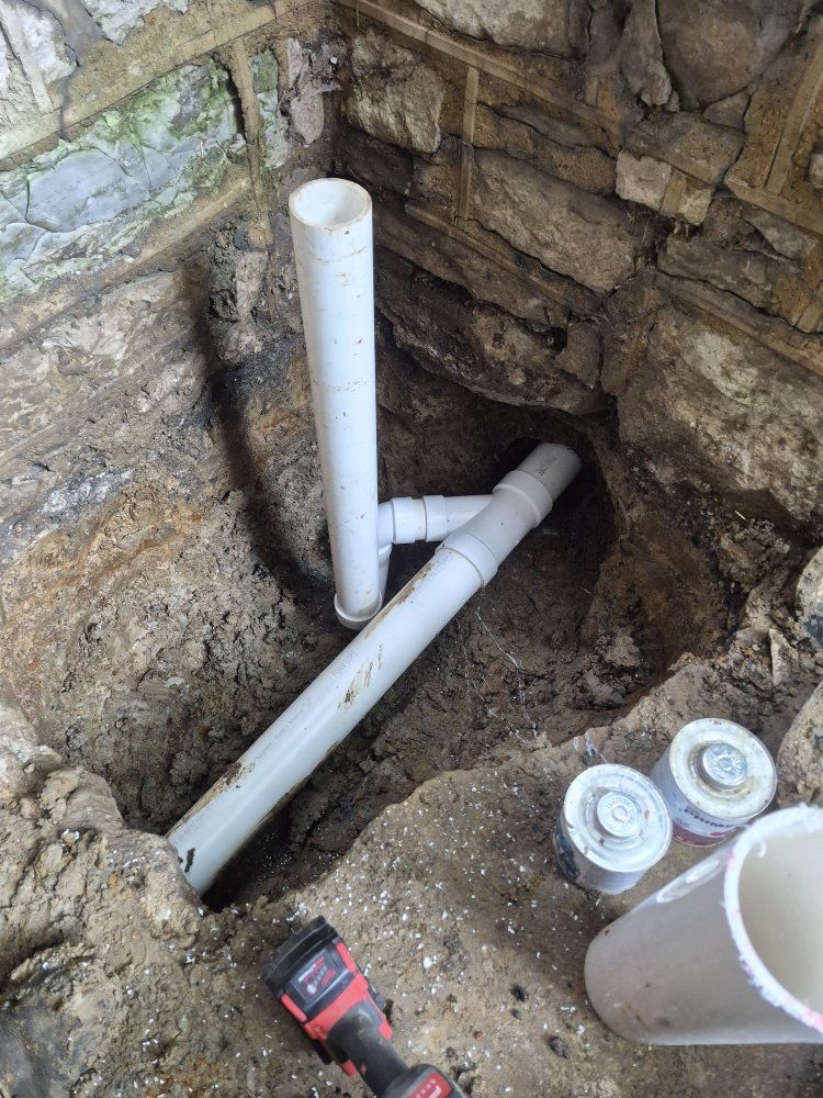 PVC pipes installed in a dug stone-lined trench beside a wall, with tools nearby