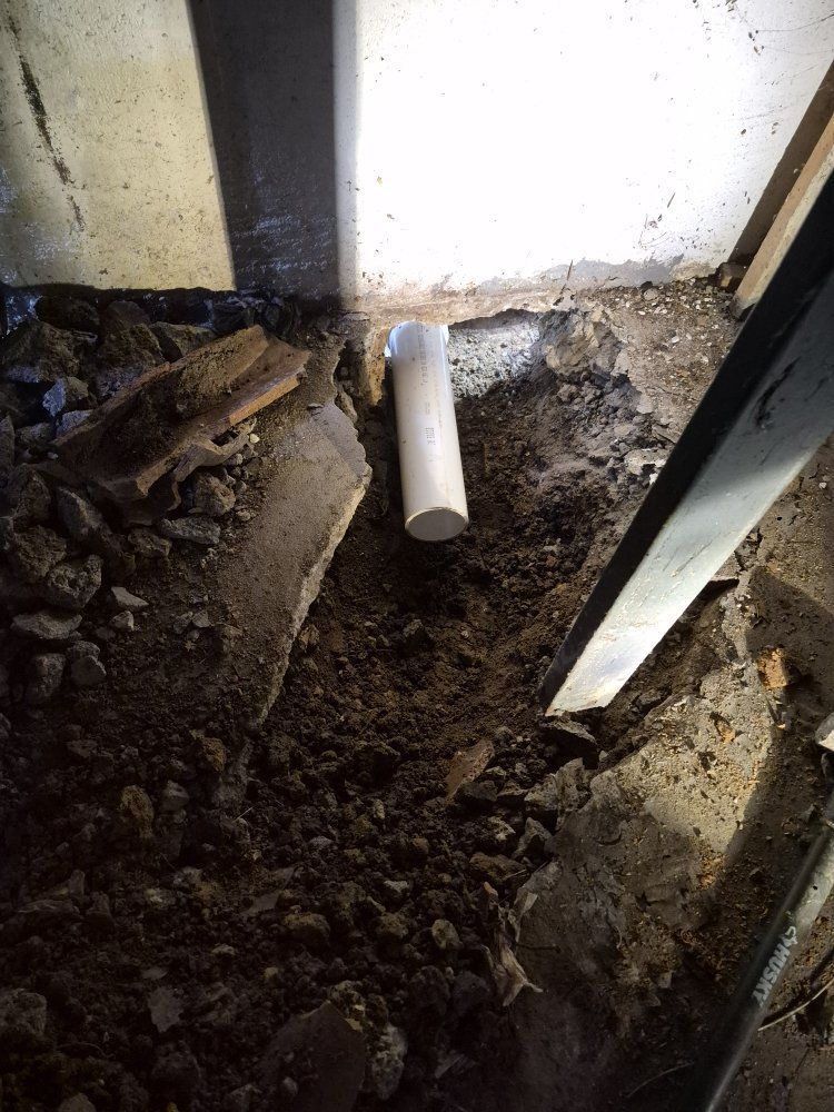 Dirt-filled crawl space with a white PVC pipe protruding from the wall and metal framing on the right.