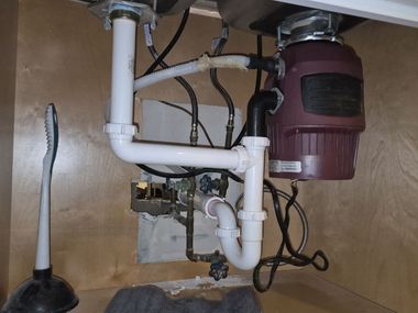 Under-sink garbage disposal and plumbing with white pipes and a red motor unit
