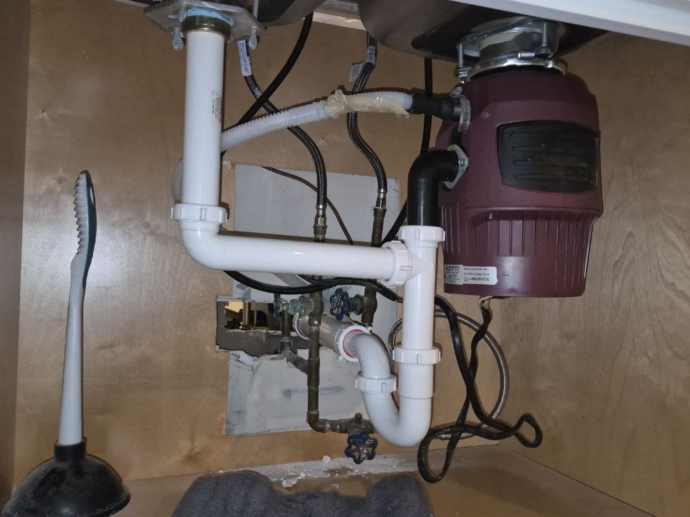 Under-sink plumbing with white PVC pipes and a red garbage disposal unit in a cabinet.